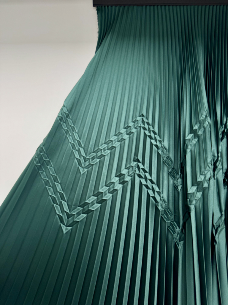 Plissé speciale su tessuto verde petrolio con pattern chevron in rilievo intrecciato tra le pieghe del tessuto
