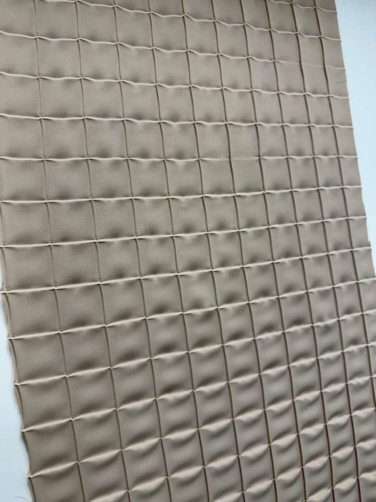Plissé piatto con pattern a griglia, pieghe incrociate su tessuto tortora