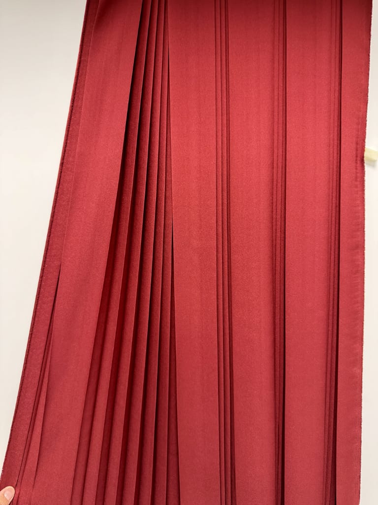 Plissé piatto su tessuto rosso, pieghe parallele verticali 