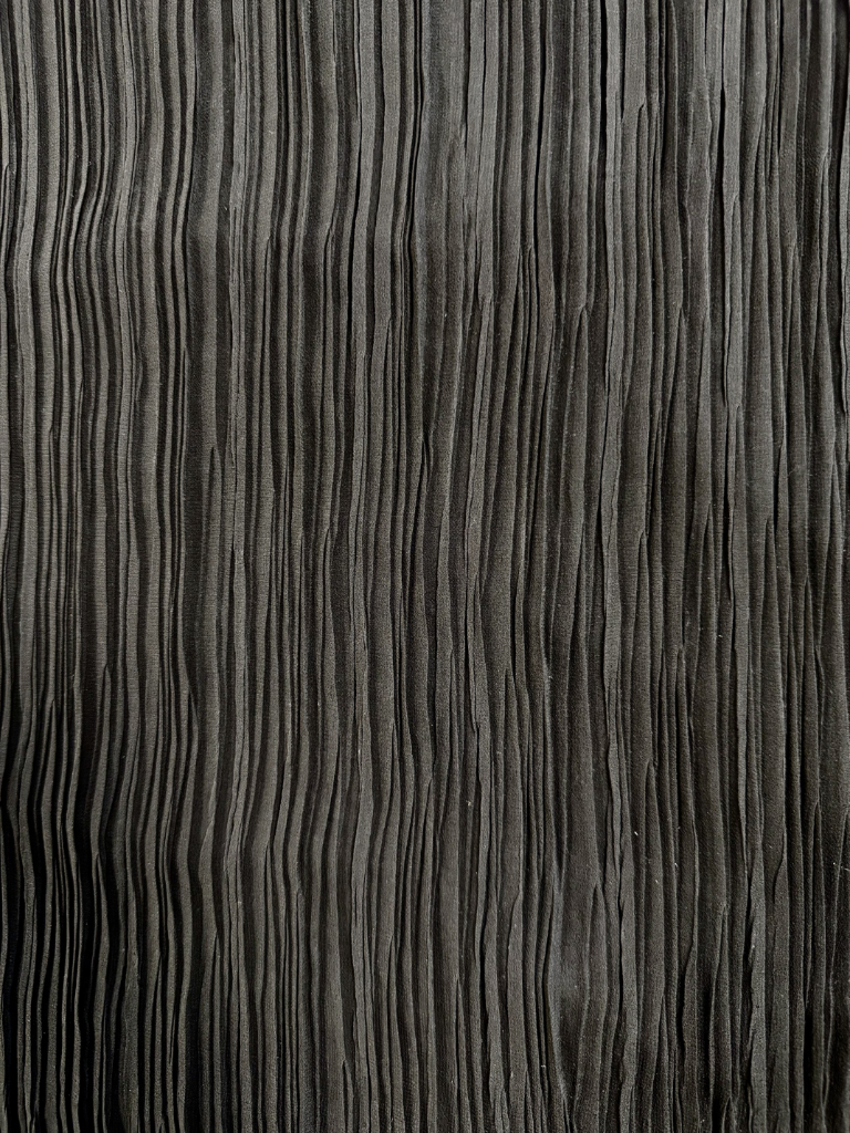 Stropicciatura tessuto grigio scuro, effetto materico verticale su tessuto di abbigliamento